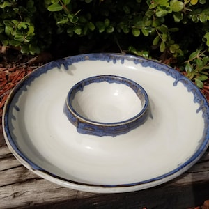 Può includere: Piatto da portata in ceramica bianca con una ciotola più piccola al centro. Il piatto ha un bordo blu e marrone.
