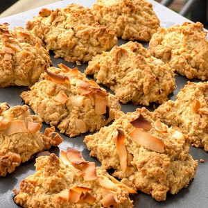May include: A baking sheet filled with golden brown coconut cookies. The cookies are topped with shredded coconut flakes.