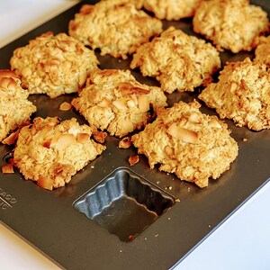 May include: A baking sheet filled with golden brown coconut macaroons. The macaroons are arranged in a circular pattern on the baking sheet. The macaroons are slightly browned on top and have a crispy texture.