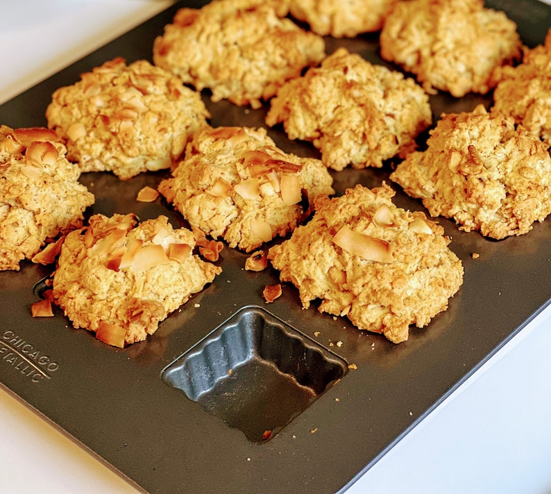 May include: A baking sheet filled with golden brown coconut macaroons. The macaroons are arranged in a circular pattern on the baking sheet. The macaroons are slightly browned on top and have a crispy texture.