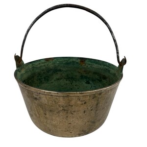 Puede incluir: Un caldero de metal vintage con un asa oscura y un interior verde. El caldero tiene un cuerpo ancho y redondeado y un asa que se arquea hacia arriba. El metal tiene un aspecto envejecido.