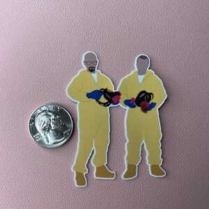 May include: Two cartoon figures wearing yellow hazmat suits and gas masks. The figures are holding red and blue objects. The figures are standing on a pink background.