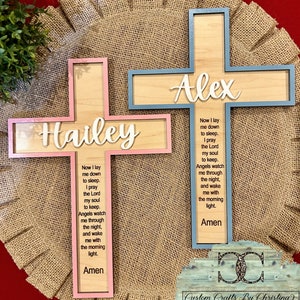 May include: Two wooden crosses with a pink and blue border. The crosses have the names "Hailey" and "Alex" on them. Each cross has a prayer inscribed on it that reads "Now I lay me down to sleep. I pray the Lord my soul to keep. Angels watch me through the night, and wake me with the morning light. Amen."
