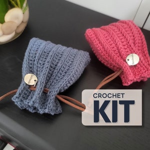 May include: Two handmade crochet items, one blue and one pink, with a leather cord and a small metal tag that says "handmade". The image also includes a sign that says "CROCHET KIT".
