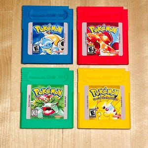 May include: Four coloured Nintendo Game Boy cartridges. The cartridges are blue, red, green, and yellow. Each cartridge features the Pokémon logo and a different Pokémon character. The cartridges are labelled "Nintendo GAME BOY".