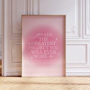 May include: A pink framed poster with a motivational quote that reads "You are the greatest project you will ever work on." The background is a gradient of pink and white with white stars.