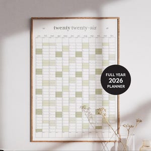 May include: A framed 2026 full-year planner with a minimalist design. The calendar grid features a light green and white colour scheme, with the text "twenty twenty-six" at the top. A black circle with white text reads "FULL YEAR 2026 PLANNER".