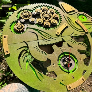 May include: A green wooden chameleon clock with gears and a clock face. The clock face has Roman numerals and black hands.