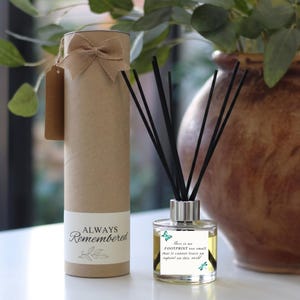 May include: A reed diffuser with black reeds in a clear glass bottle featuring a label that reads, There is no FOOTPRINT too small that it cannot leave an imprint on this world, alongside a cylindrical kraft paper gift tube with a burlap bow.