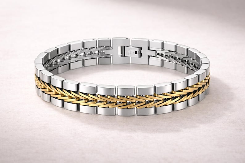 May include: A silver and gold-tone bracelet. The bracelet has a rectangular link design with a central band of interwoven gold-tone links. The clasp is silver-tone. The bracelet is a piece of jewellery.