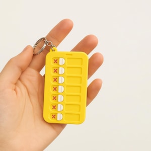 May include: Yellow pill keychain with a red X on each pill. The keychain has a silver ring.