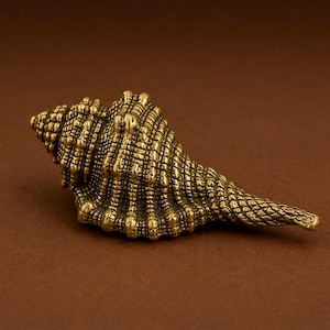 May include: A detailed, golden-colored seashell sculpture with a textured surface. The sculpture is set against a brown background, highlighting its intricate design and natural form. The seashell's spiral shape and detailed ridges are clearly visible.