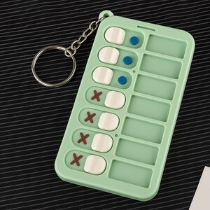 May include: A mint green pill organizer keychain with a silver key ring. The organizer has eight compartments, each with a white pill and a red X or a blue dot.