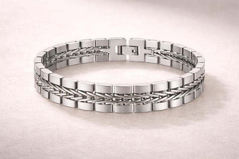May include: A silver bracelet with a geometric design. The bracelet features rectangular links connected by a woven pattern. The clasp is a simple, secure design. The jewellery is displayed on a light background.