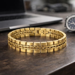 May include: A gold-coloured bracelet with a rectangular link design. The bracelet is made of metal and has a secure clasp. A wristwatch with a blue face is visible in the background. The bracelet is approximately 20 cm in circumference.