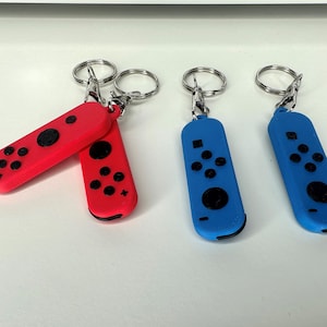 May include: Three keychains shaped like Nintendo Switch Joy-Cons. Two are red and one is blue.