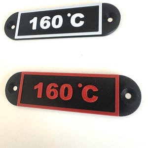 May include: Two black oval temperature labels, each displaying "160 °C". One has white text and a white border, the other red text and a red border. Both labels have two holes for mounting.