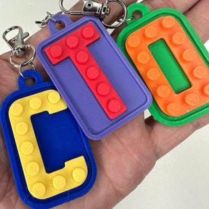May include: Three colourful keychains shaped like letter blocks. The letters are C, T, and O. The C is blue with yellow dots, the T is purple with red dots, and the O is green with orange dots.