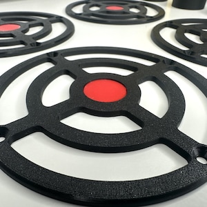 May include: A collection of circular black speaker grilles featuring a textured finish and a central red circular insert. Each grille has a frame with four mounting holes positioned at equal intervals around the outer edge of the circular structure.