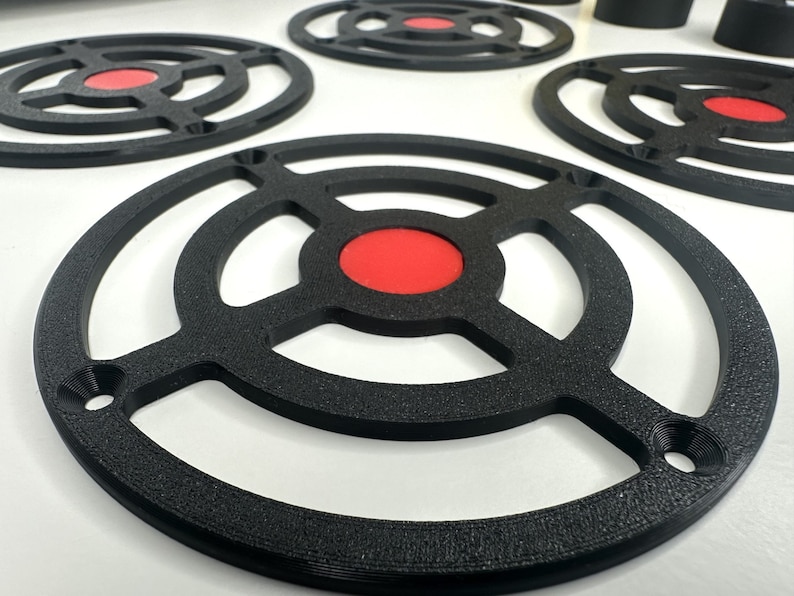 May include: A collection of circular black speaker grilles featuring a textured finish and a central red circular insert. Each grille has a frame with four mounting holes positioned at equal intervals around the outer edge of the circular structure.