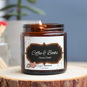 May include: A lit scented candle in a brown glass jar with a label that reads "Coffee & Books." The candle sits on a wooden slice. A small glass jar with matches is in the background.