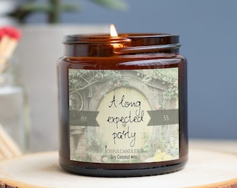 May include: A lit brown glass jar candle with the text "A long expected party" on a label featuring a whimsical door design. The candle sits on a wooden slice, with matches in a glass jar in the background.