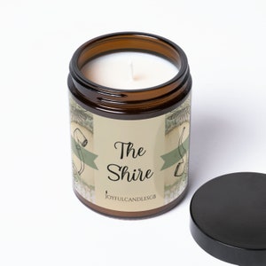 Peut inclure: Un bocal en verre brun contenant une bougie blanche. Le bocal est &eacute;tiquet&eacute; "The Shire" avec un ruban vert et un dessin d'une pipe et d'un seau. L'&eacute;tiquette indique &eacute;galement "JoyfulCandlesGB".