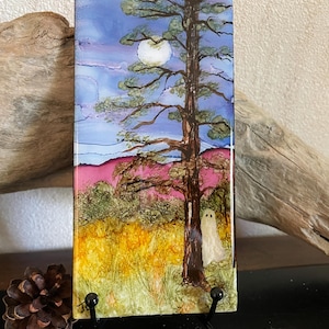 May include: A rectangular tile featuring an alcohol ink painting of a tall pine tree in a field under a full moon. A small white ghost figure stands near the tree trunk. The scene includes vibrant yellow grass, pink hills, and a blue sky.