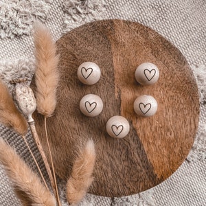 Op de afbeelding: Zes houten hartvormige ornamenten met een lichtbruine afwerking en een wit hartontwerp op elk. De ornamenten zijn gerangschikt op een houten dienblad met een bruine afwerking.