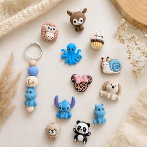 Könnte beinhalten: Eine Sammlung kleiner, bunter Silikonanhänger in Form eines Igels, Hirsches, Cupcakes, Oktopus, einer Schnecke, Mausohren mit Leopardenmuster, eines Hundes, eines blauen Aliens, Pandas und Otters. Ein Schlüsselanhänger mit Holzperlen ist dabei.