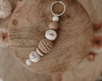 May include: A wooden keychain with a crocheted bead, a heart bead, and a bead with the name "Carla" engraved on it.