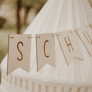 May include: A wooden banner with the word "SCHOOL" spelled out in gold letters. The banner is hanging from a white tent.