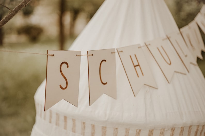 May include: A wooden banner with the word "SCHOOL" spelled out in gold letters. The banner is hanging from a white tent.