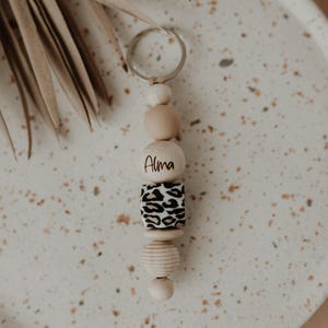 Può includere: Un portachiavi in legno con un ciondolo a stampa leopardata e un perno in legno con il nome "Alma" inciso.