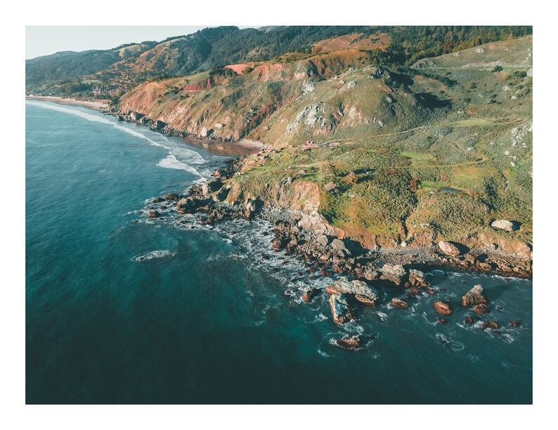 May include: Aerial view of a rocky coastline with turquoise water crashing against the shore. Lush green hills and cliffs rise up in the background.