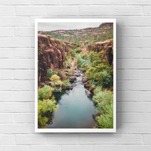 May include: A scenic view of a narrow canyon with a winding river flowing through it. Lush green trees and foliage line the riverbanks, while the canyon walls are a reddish-brown color.