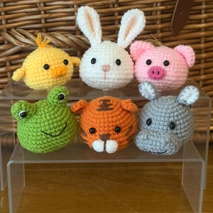 Può includere: Sei teste di animali all'uncinetto fatte a mano: un pulcino giallo, un coniglietto bianco, un maiale rosa, una rana verde, una tigre arancione e un ippopotamo grigio. Ognuno ha occhi di sicurezza neri ed è esposto su un supporto in acrilico trasparente.