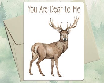 Puede incluir: Una tarjeta de felicitación blanca con una ilustración en acuarela de un ciervo marrón con grandes astas. El texto "You Are Dear to Me" está impreso en marrón en la parte superior. La tarjeta está sobre un sobre beige claro a juego.