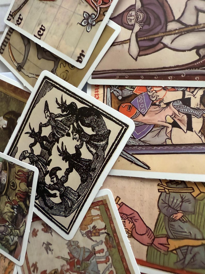 May include: A collection of vintage tarot cards with detailed illustrations. The cards feature images in shades of brown, black, red, and purple. The artwork depicts figures, scenes, and symbols, with white borders. The cards are arranged in a scattered layout.