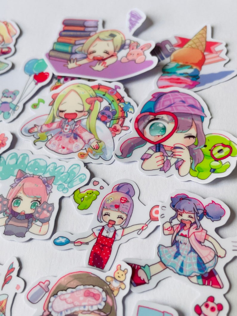 May include: A collection of colourful stickers featuring cartoon characters with different expressions and poses. The stickers are on a white background and include a girl reading a book, a girl with a magnifying glass, a girl with a lollipop, and a girl with a cat.