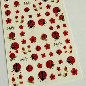 May include: A sheet of ladybug and flower stickers. The stickers feature red ladybugs with black spots and red flowers. The word "Ladybug" is written in a cursive font on the sheet. The stickers are on a white background.