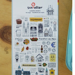 K&ouml;nnte beinhalten: Eine Bogen mit Aufklebern, die Illustrationen deutscher Sehensw&uuml;rdigkeiten zeigen, darunter Schloss Neuschwanstein, die Skyline von Frankfurt am Main und ein traditionelles deutsches Bierkrug. Die Aufkleber sind auf wei&szlig;em Papier mit schwarzen Linien gedruckt.