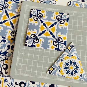 May include: A close-up of two blue and yellow patterned tiles, one square and one triangular, on a gray cutting mat. The tiles have a floral design with blue, yellow, and white accents.