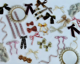 Könnte beinhalten: Eine Sammlung dekorativer Aufkleber mit verschiedenen Schleifendesigns in Braun-, Rosa- und Cremetönen. Enthält Samt-, gemusterte und Satin-Schleifen sowie perlenbesetzte Kreise und Bänder. Eine kleine Cherub-Statue ist ebenfalls vorhanden.