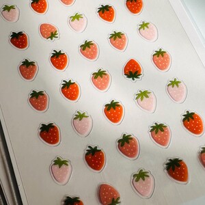 May include: A sheet of stickers featuring a repeating pattern of red and pink strawberries. The strawberries are outlined in black and have green leaves.