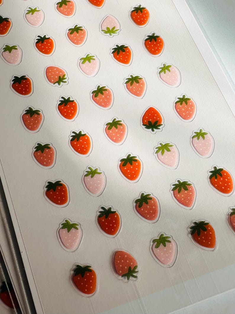 May include: A sheet of stickers featuring a repeating pattern of red and pink strawberries. The strawberries are outlined in black and have green leaves.