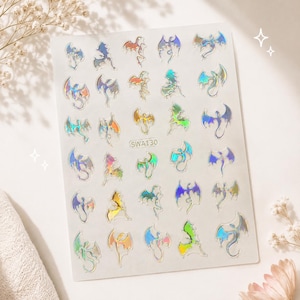 May include: A rectangular sheet of adhesive nail decals featuring various small dragon silhouettes. The stickers have a holographic finish that reflects multiple colours. The text SWA130 is printed in the centre of the white backing sheet.