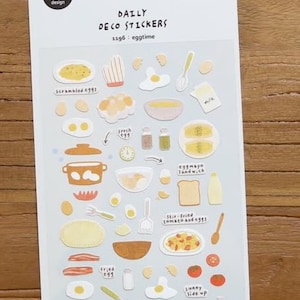 Op de afbeelding: Een vel Daily Deco Stickers met illustraties met een ontbijtthema. De stickers bevatten afbeeldingen van roerei, gebakken eieren, eiersandwiches en spiegeleieren. De tekst op het vel luidt "DAILY DECO STICKERS 1196: eggtime".