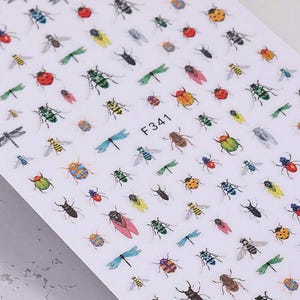 Puede incluir: Hoja de pegatinas para uñas con varios insectos, incluyendo libélulas, mariquitas y escarabajos. Los insectos son de varios colores, como verde, rojo, amarillo y azul. La hoja tiene el número "F341" impreso.