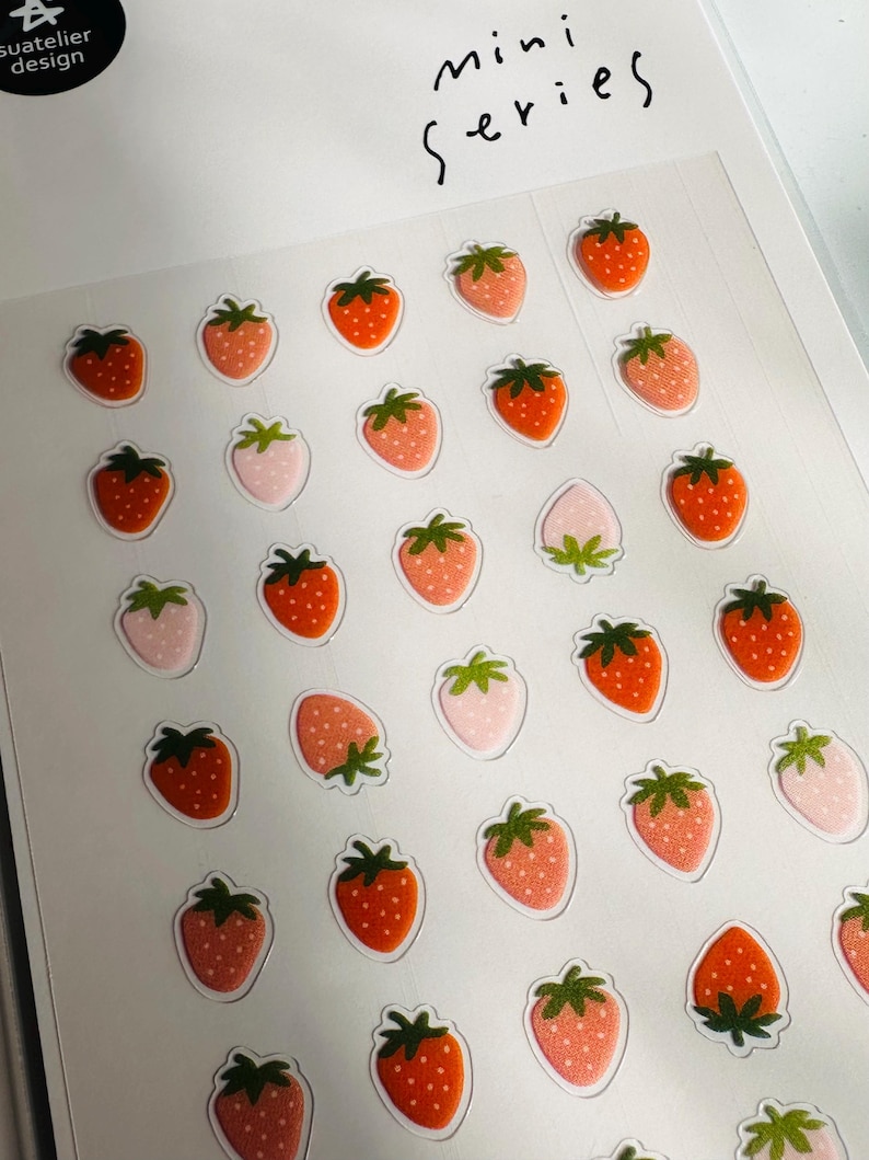 May include: A sheet of stickers featuring a variety of strawberry designs. The strawberries are in shades of pink, red, and green. The sheet is labeled "mini series".